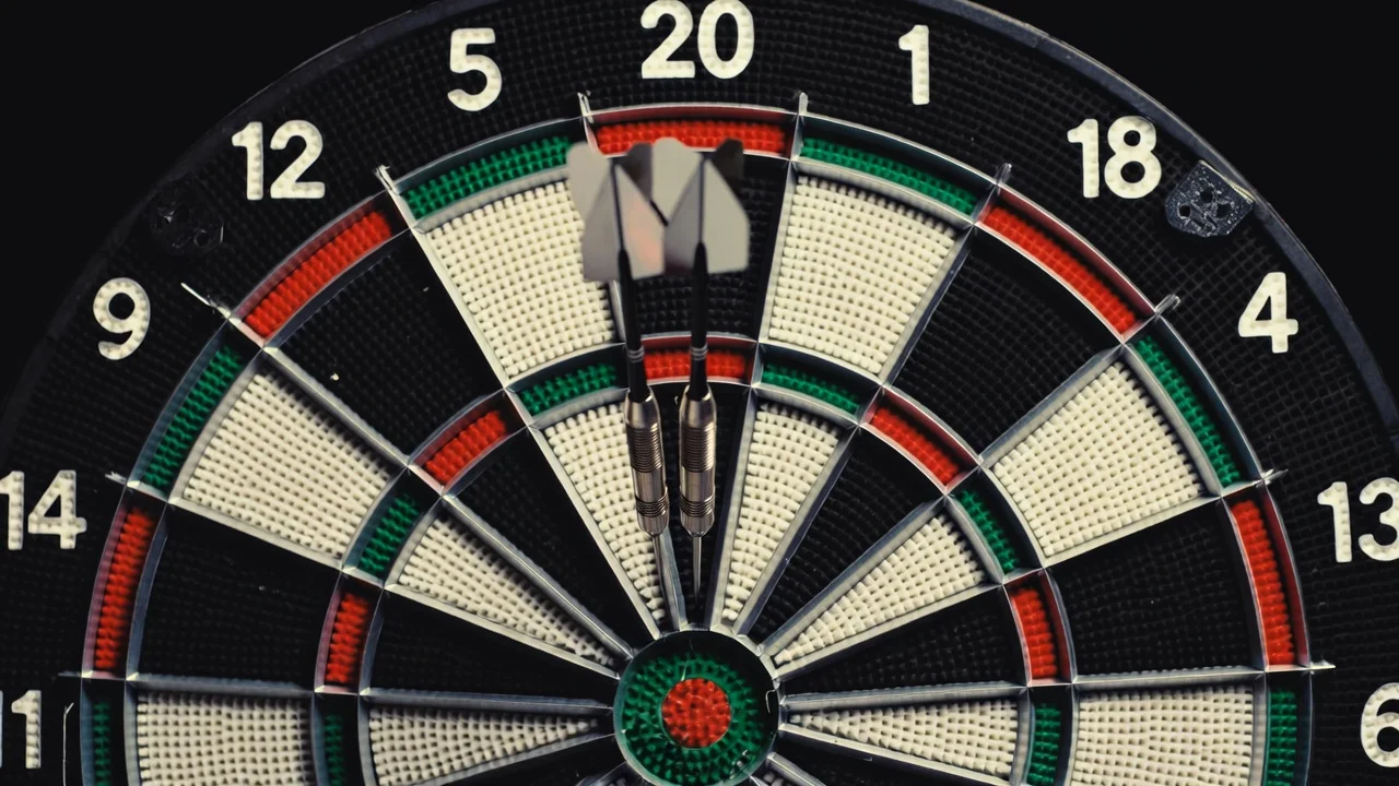 Nahaufnahme einer Dartscheibe mit drei Pfeilen im Triple-20-Feld unter Spotlicht